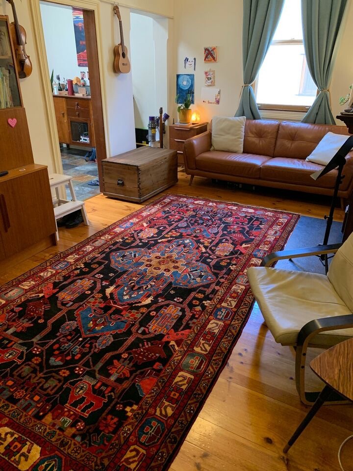 Hand-woven tribal Persian rug with intricate geometric patterns and bright colors on display in a well-lit room.