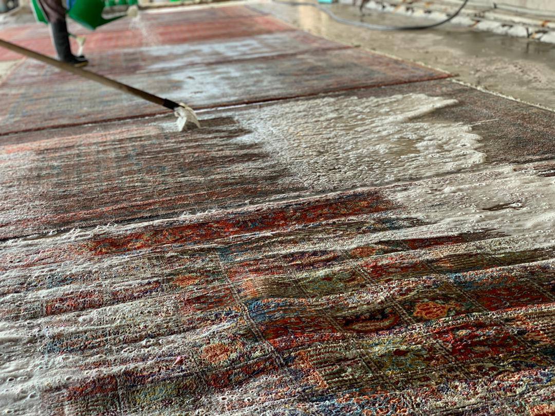 A person using a vacuum cleaner to clean a Persian rug. The rug has intricate designs and vibrant colors, and the person is using a special attachment to gently remove dirt and debris from the fibers.