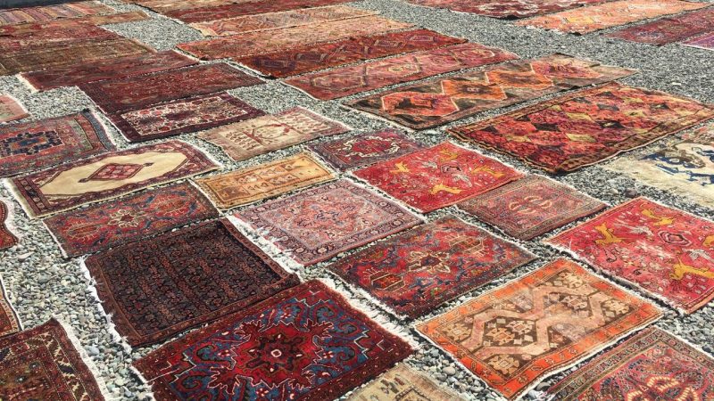 close-up shot of a beautiful handmade Persian rug. The rug's intricate design is visible, featuring a mix of vibrant colors and patterns. The rug is positioned on a hardwood floor, surrounded by